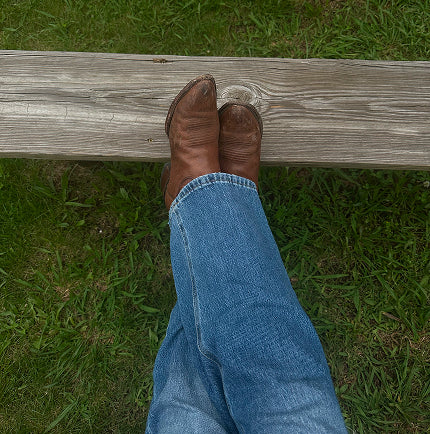 Grounded western boots on wood and grass, symbolizing a life of intentional living and connection to earth and spirit.