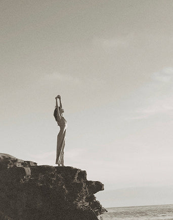 Woman standing on a cliff overlooking the ocean with a cloudy sky. for 'Create Your Own Mantra Board' to inspire self discovery