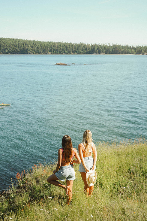 Two women sitting on a grassy hill overlooking a lake, for 'Create Your Own Mantra Board' to inspire self discovery