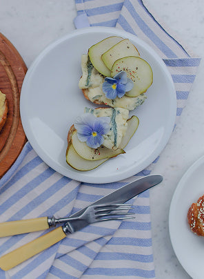 Plated dish with sliced pears and edible flowers on a striped tablecloth, for 'Create Your Own Mantra Board' guided self discovery
