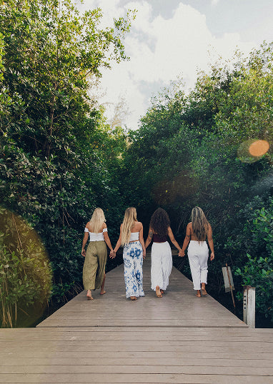 Four women walking hand in hand on a wooden path surrounded by greenery, for 'Create Your Own Mantra Board' guided self discovery tool