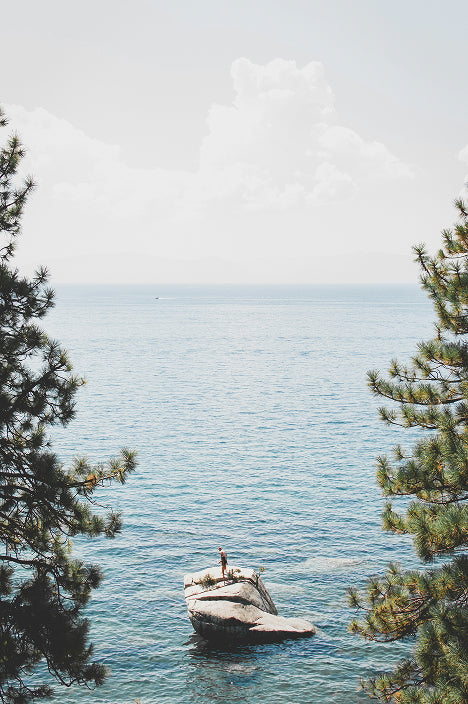 Person standing on a rock in the middle of a lake with trees on either side. For 'Create Your Own Mantra Board' to inspire self discovery.