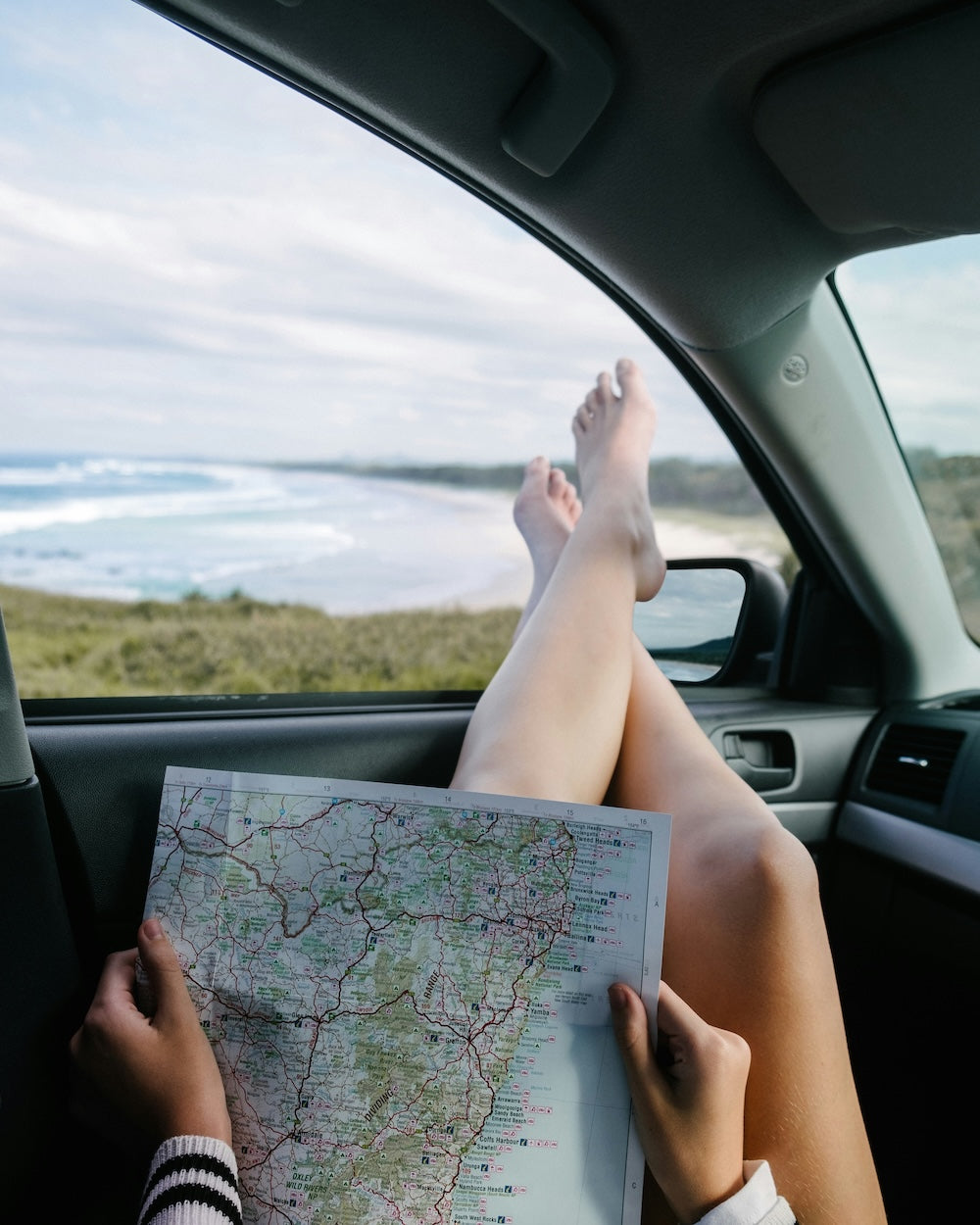 Person sitting in a car by the sea, holding a map. For 'Create Your Own Mantra Board' to inspire self discovery.